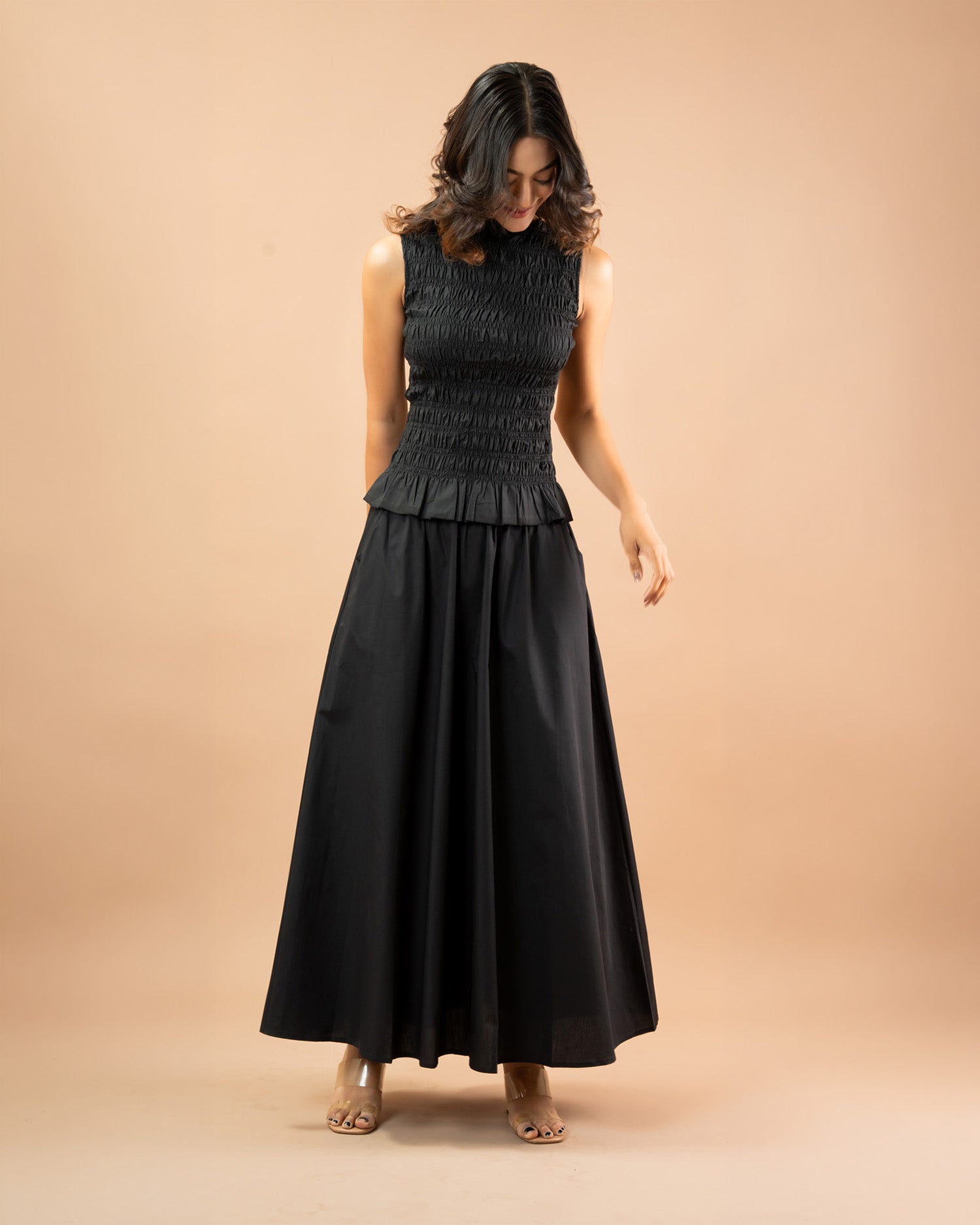 Woman wearing a black sleeveless dress with a peplum waist on a beige background