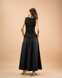 Woman wearing a black dress with a textured bodice and plain skirt on a beige background