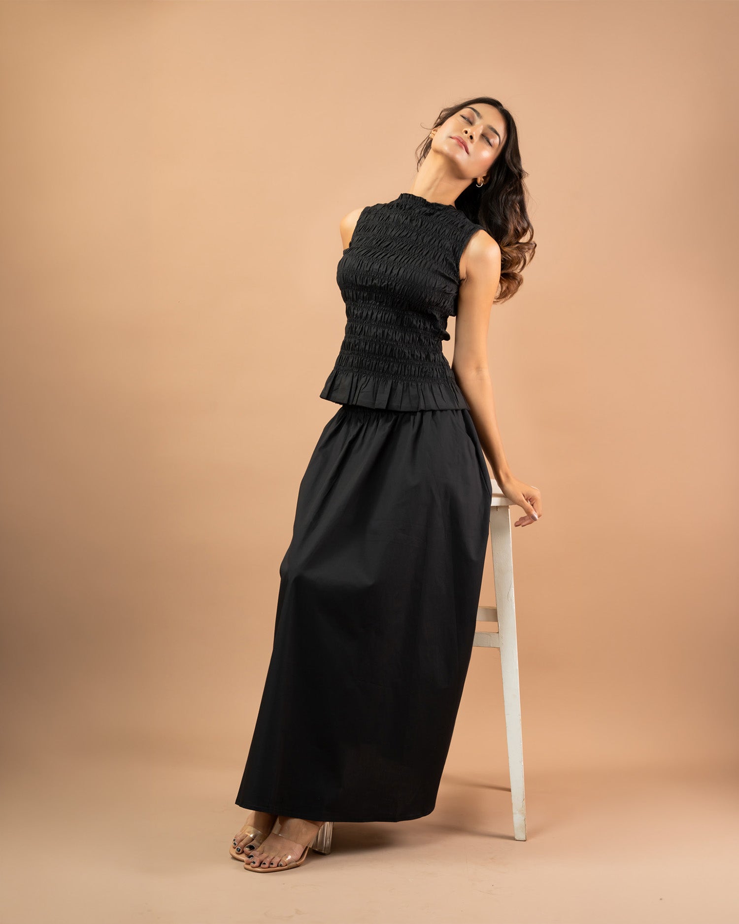 Woman wearing a black sleeveless top and long skirt against a beige background