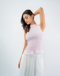 Woman wearing a pink sleeveless top and white pants against a white background