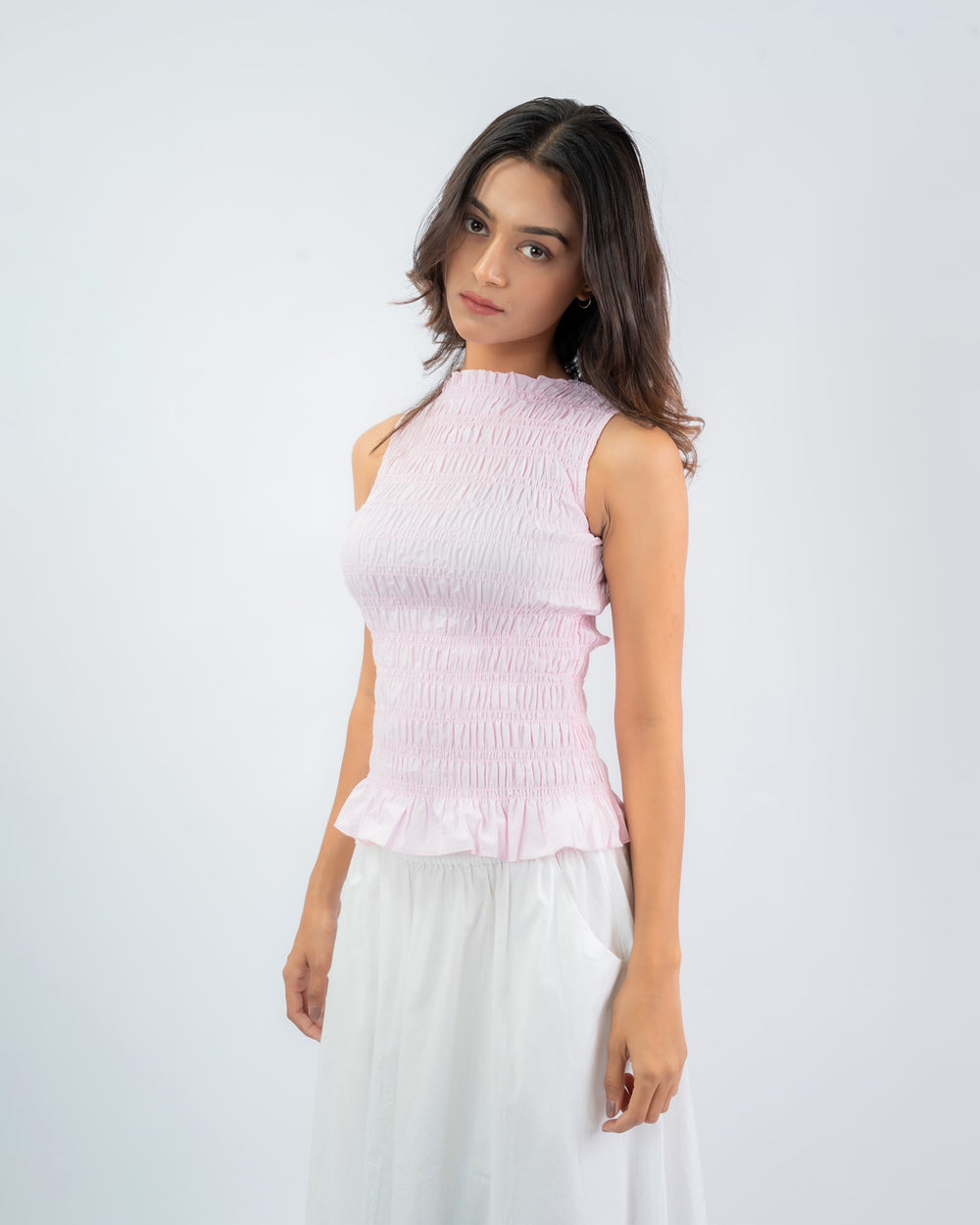 Woman wearing a pink sleeveless top and white pants on a white background
